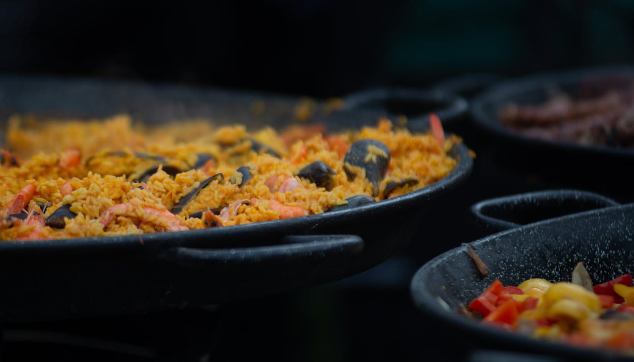 about-us Appetizing close-up of traditional seafood paella cooking in a large outdoor pan.